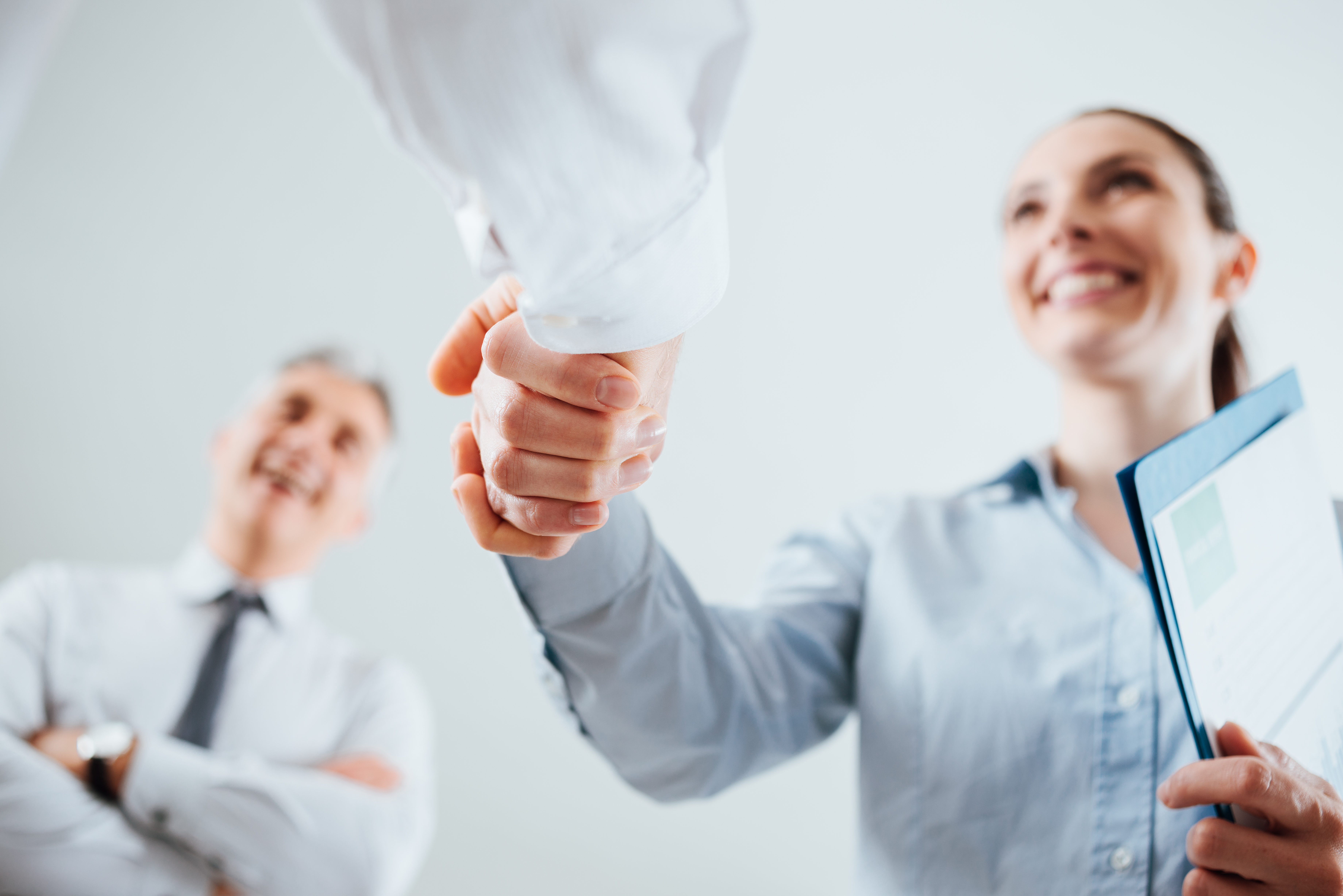 low angle shot of a business woman shaking hands with another business person, and they are smiling
