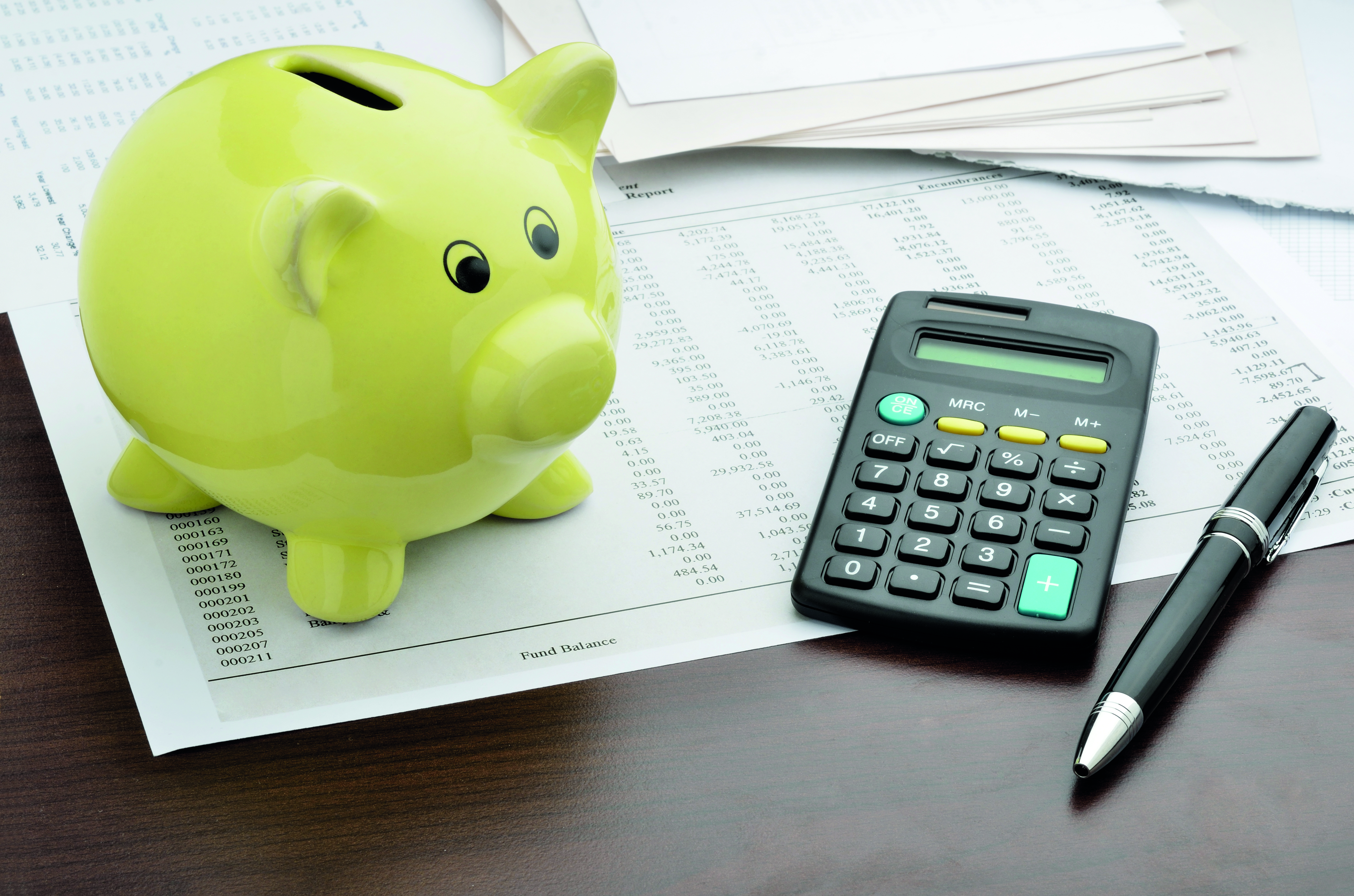 a green piggy bank, a calculator and a pen on top of paperwork 