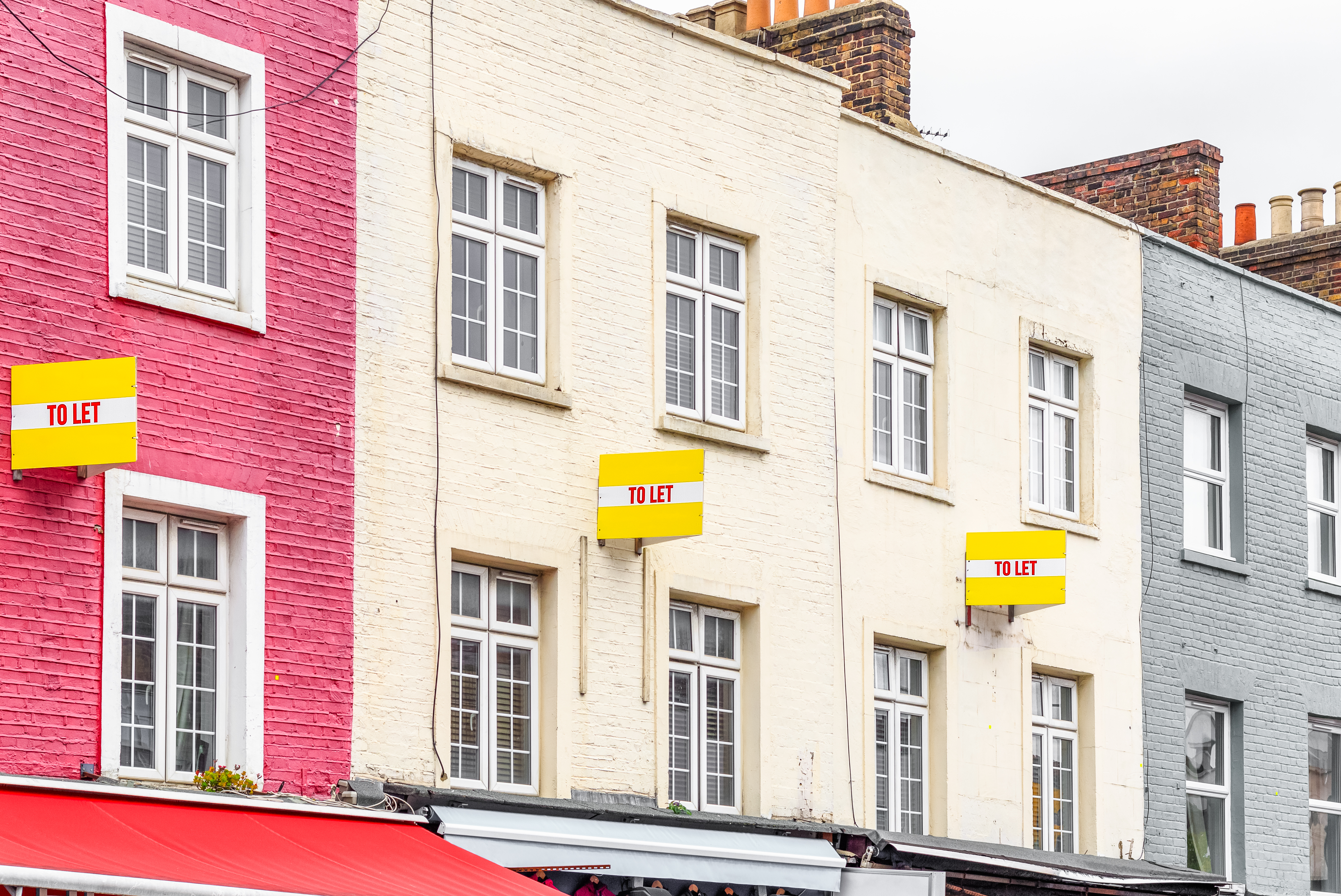 a row of flats on a UK street with a yellow sign on each wall that reads 'To let'