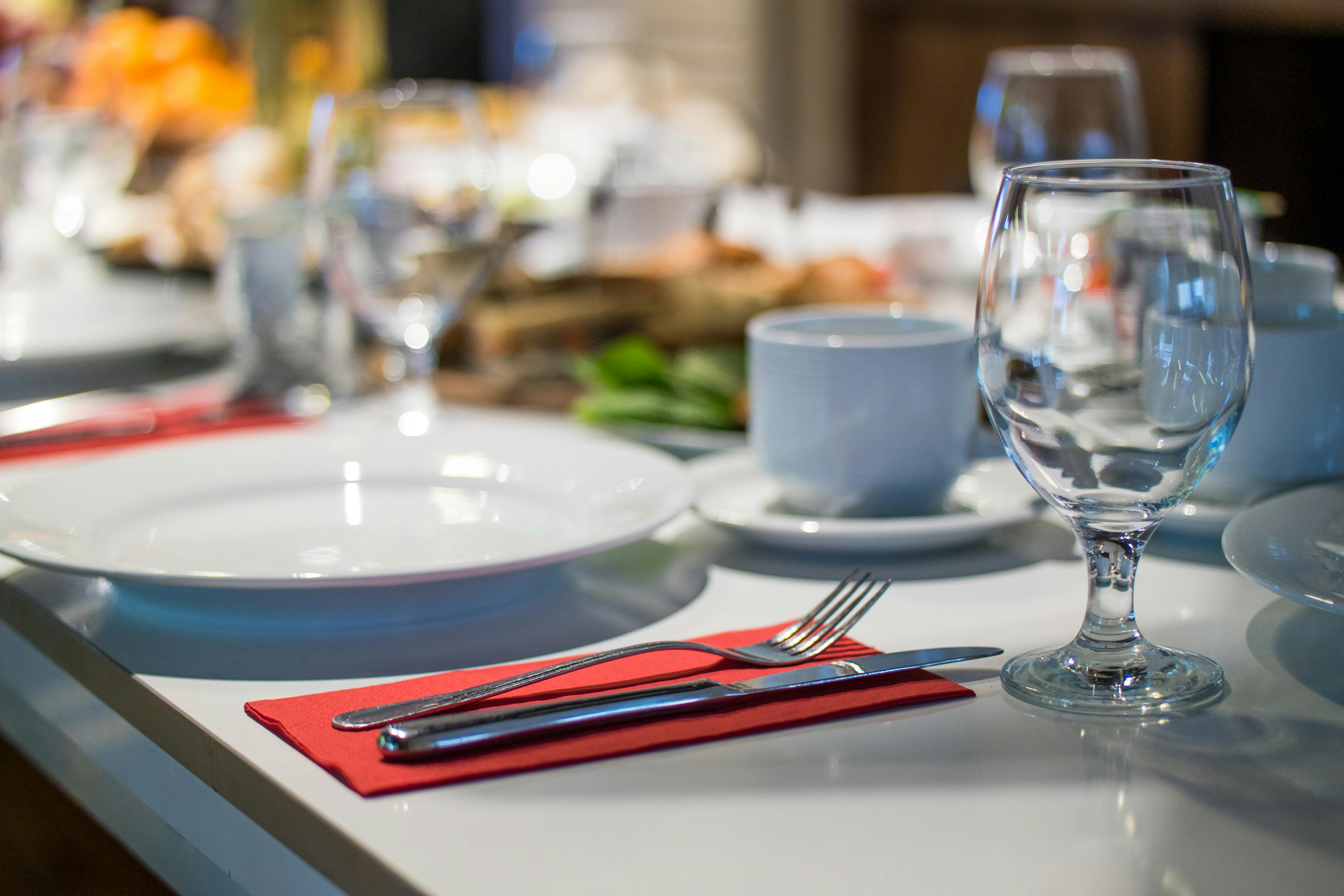Close-up of a dining table set with white plates, glassware, a coffee cup, and silver cutlery placed on a red napkin.