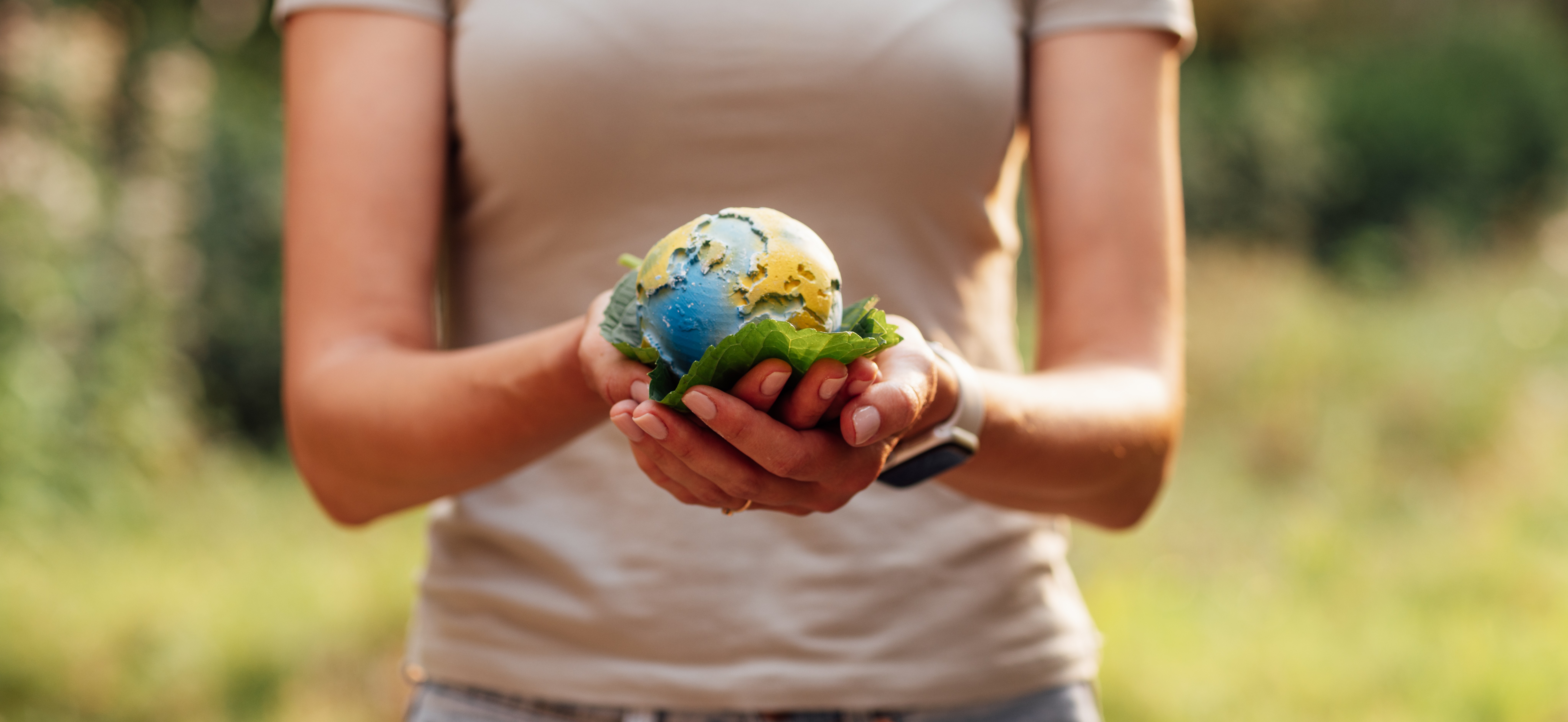 A person holds a small globe resting on green leaves, symbolizing environmental care. The background is a blurred, lush natural setting, creating a peaceful tone.