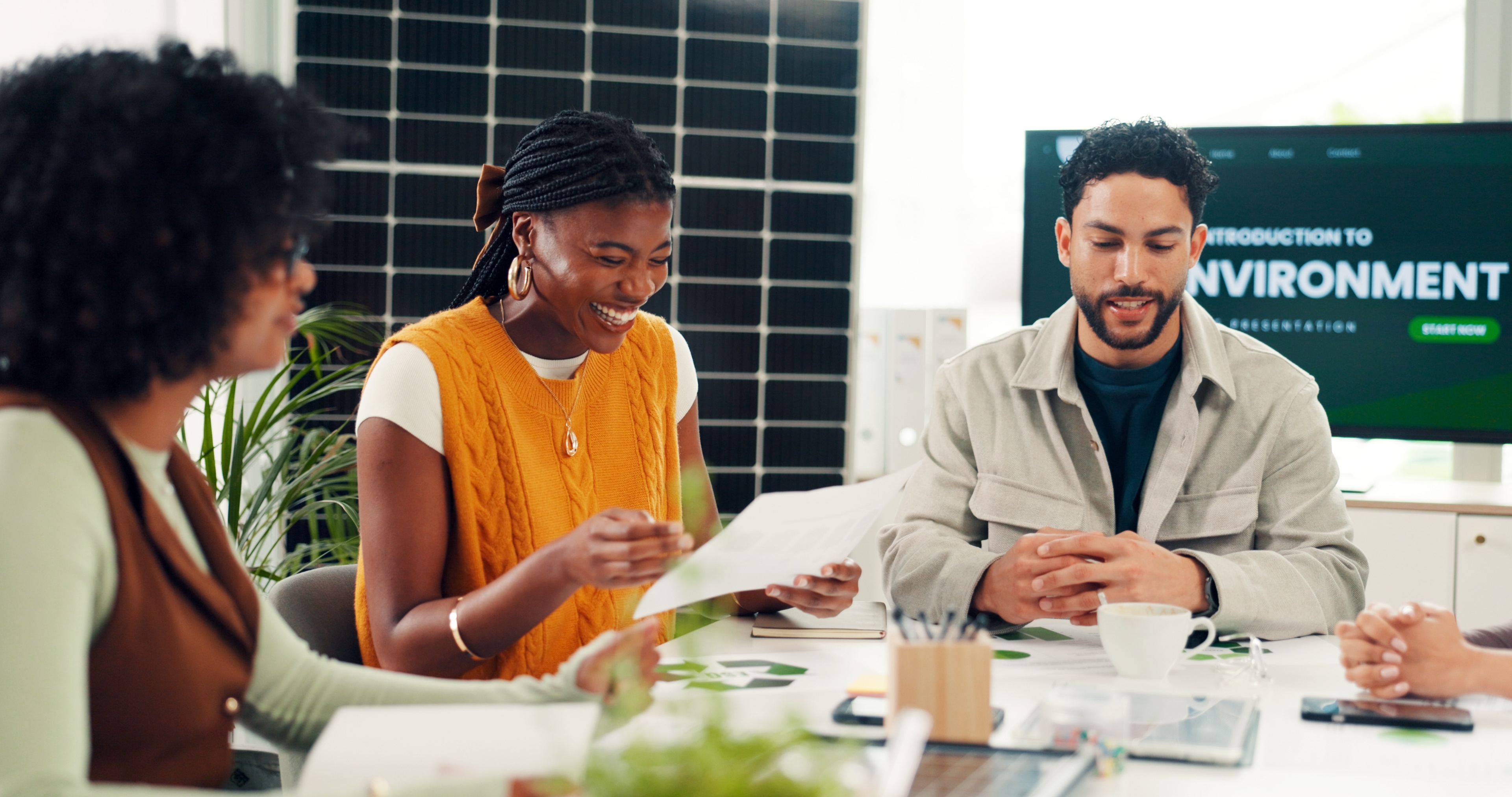 A diverse team of professionals smiling and reviewing documents together during an environmental presentation in a modern office with a solar panel background.