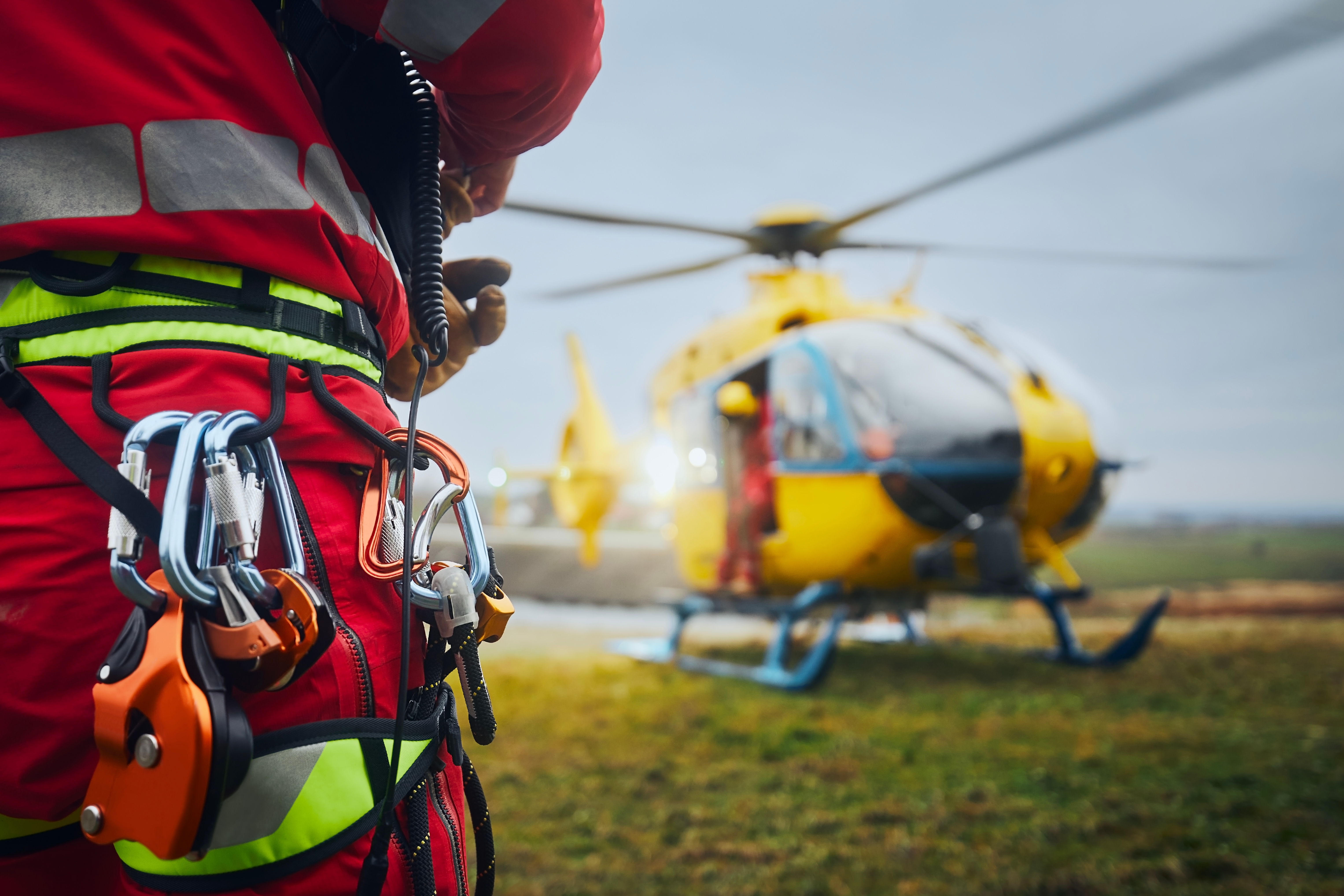 Emergency rescue worker wearing safety equipment beside a rescue helicopter.