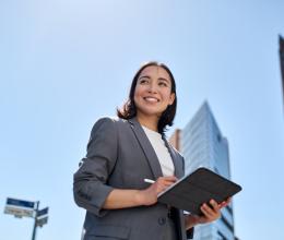 businesswoman proudly looking up with a tablet in hand, in a business city area