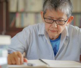Older gray hair woman writer thoughtfully handwriting testament. Senior Asian woman sitting in home book library taking notes on a notebook, writing diary or biography. Elderly women prepare a will.