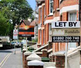 Terraced houses on a residential street with two letting agent signs up, one of them says 'Let by Randalls' and the other is 'Brettsletts To Let"
