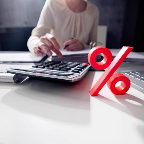 work desk with laptop and calculator, person working on it, and a red percentage symbol on the table