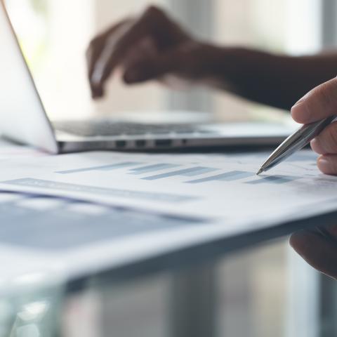 Businessman with pen in hand working on laptop computer reviewing business marketing report