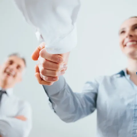 low angle shot of a business woman shaking hands with another business person, and they are smiling