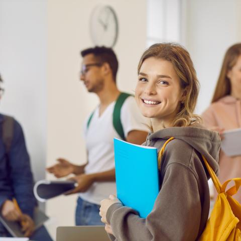 school student holding books and smiling at camera in a school full of other students