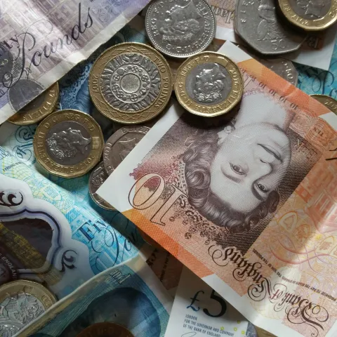 a table with British pound bank notes spread out and coins resting on top of it