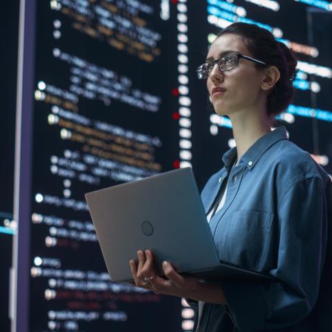 woman holding a laptop with a screen full of code written around her