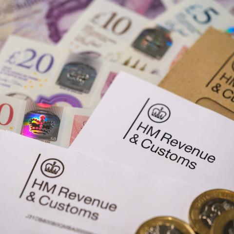 A close-up of HM Revenue & Customs documents surrounded by British currency, including £50, £20, and £10 banknotes, as well as £1 coins