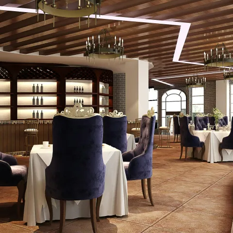 Elegant restaurant interior with luxurious dark blue velvet chairs around round tables covered in white tablecloths, warm wooden ceiling beams, chandeliers, and large windows allowing natural light to fill the space.