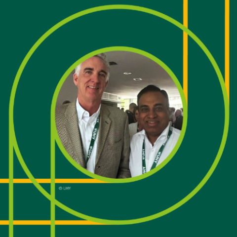 Two men wearing UHY lanyards stand side by side, smiling at the camera in a professional indoor setting. The photo is framed within overlapping green and yellow circles on a dark green background with a © UHY watermark.