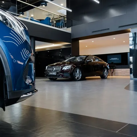 Sleek showroom featuring three luxury cars: blue, black, and white, with a modern, sophisticated atmosphere and bright lighting.