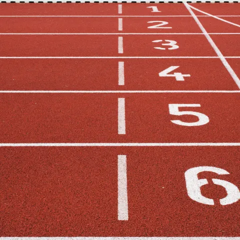 Red running track with white numbered lanes from 1 to 6, ending at a checkered finish line. The scene conveys anticipation and athletic readiness.