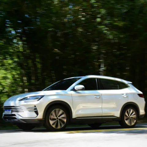 A silver SUV drives along a tree-lined road, with blurred greenery in the background, suggesting motion and a sense of speed and freedom.