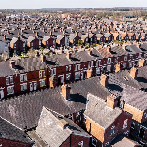 Aerial view of a densely packed, uniform row of red brick terraced houses with dark roofs, stretching into the distance.