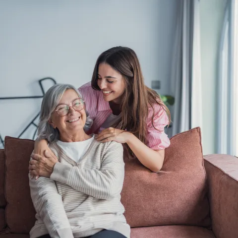 A young woman embraces her mature mother or grandmother at home, enjoying a quiet and loving moment together that reflects emotional connection, care, and family bonding between generations.