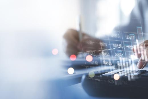 Businessperson using a calculator with pen and financial documents, overlaid with digital graphs and stock market data visuals, representing financial analysis or accounting work