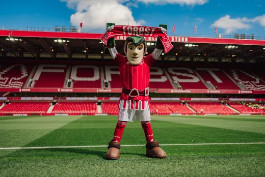 Nottingham forest mascot standing in their stadium with a scarf stretched above his head